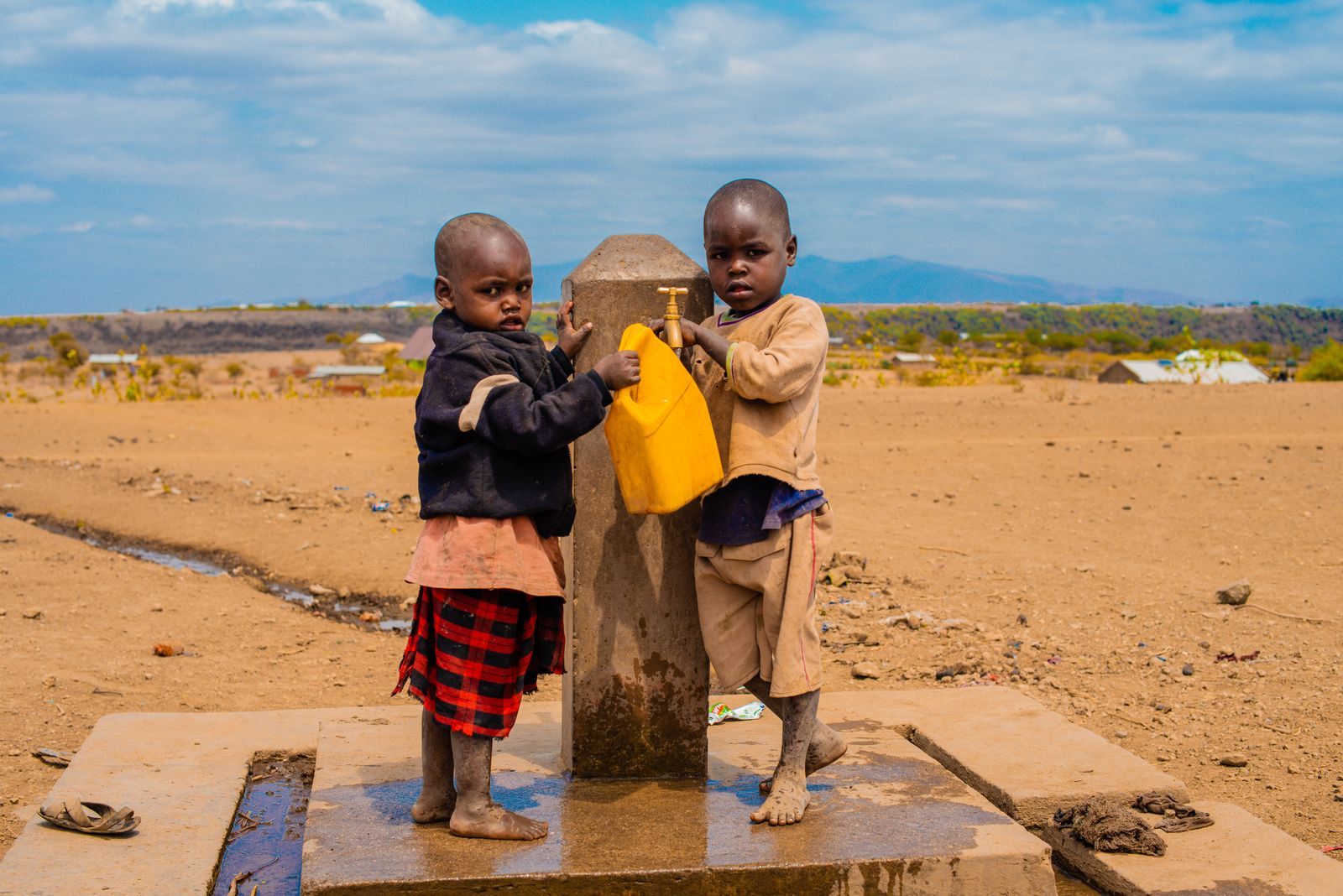 Two children filling a yellow water can at a new well pump