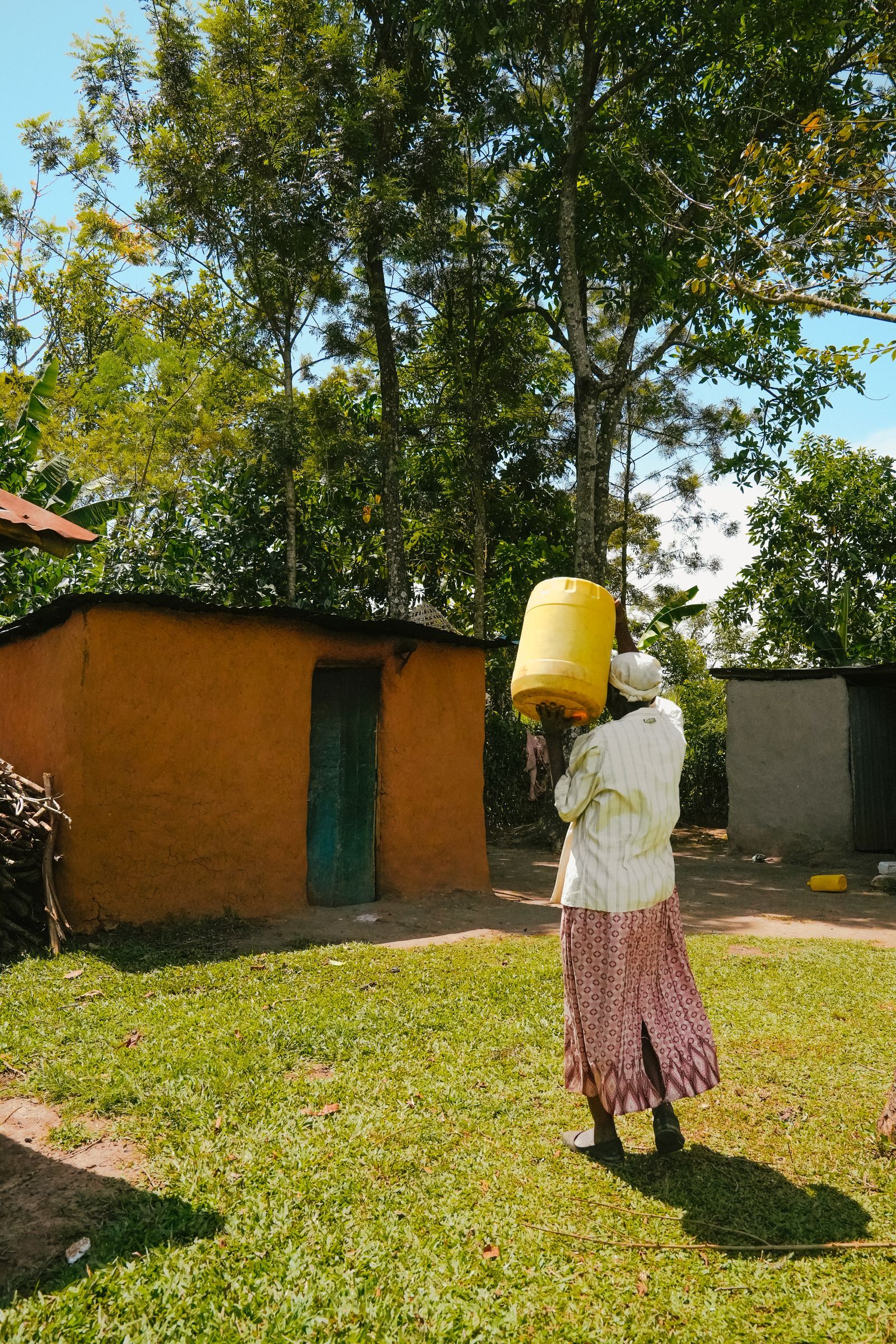 A woman carrying a water can across a yard