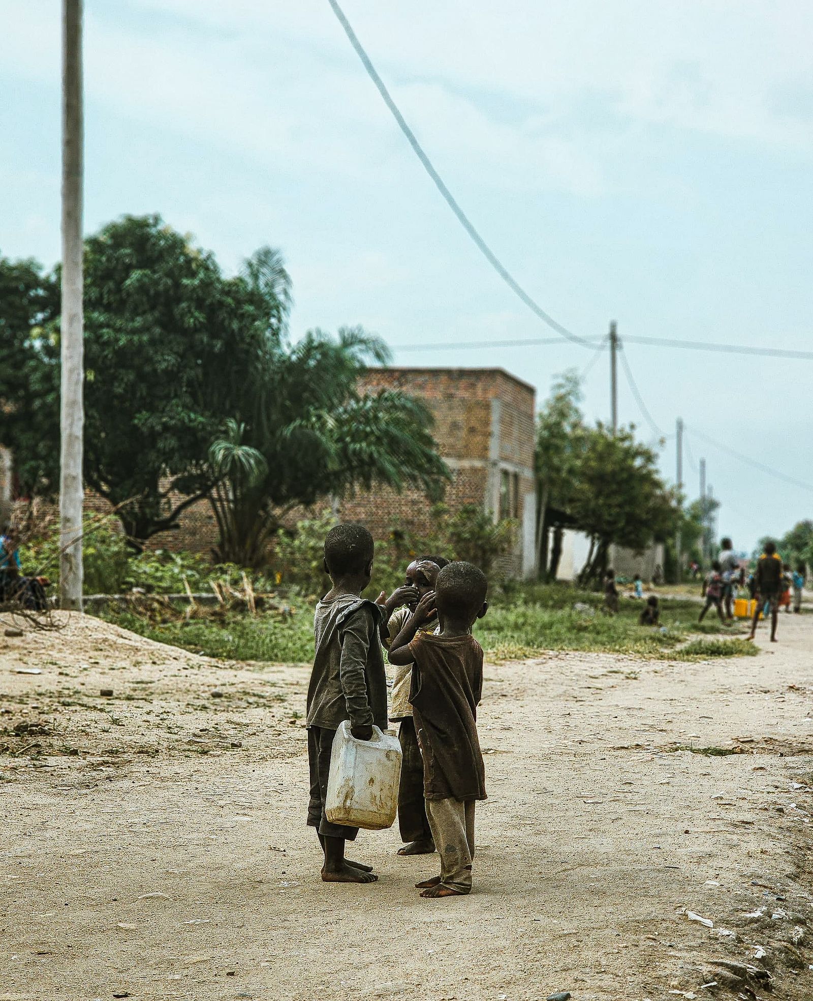 Two children walking down a dusty road with water
